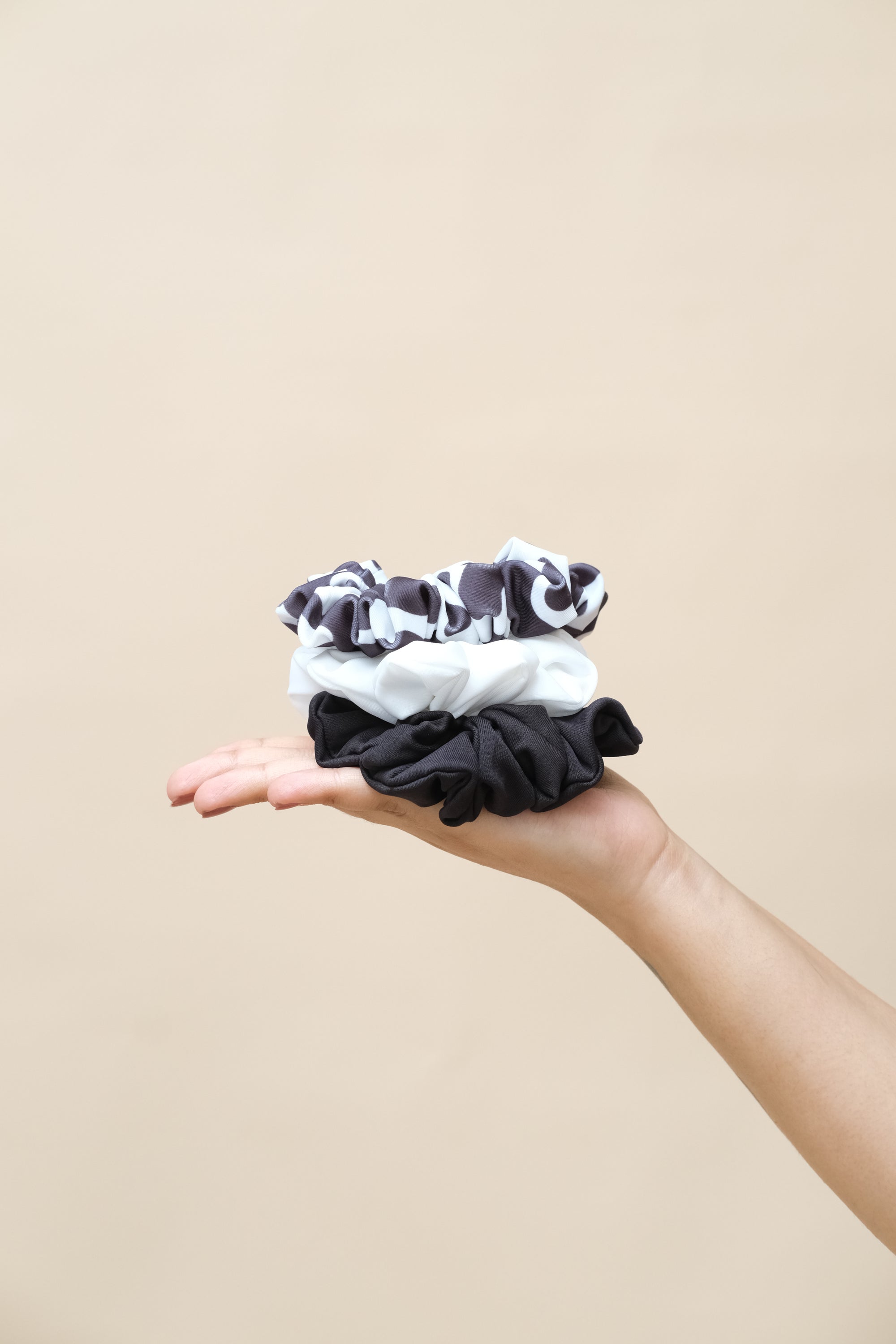 Hand holding three black and white patterned scrunchies 