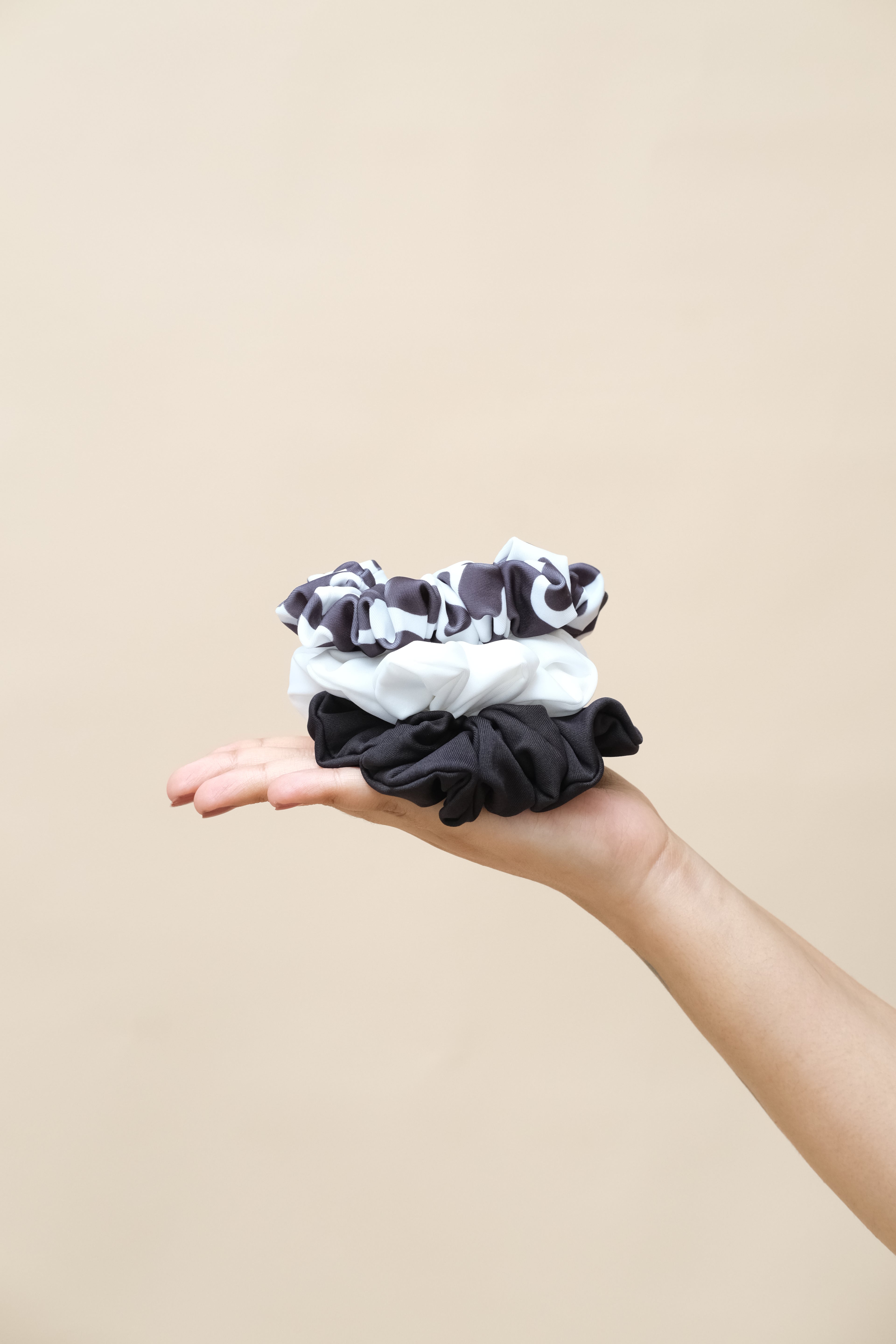Hand holding three black and white patterned scrunchies 