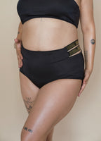 Woman wearing black high-waisted bikini bottoms with a beige background
