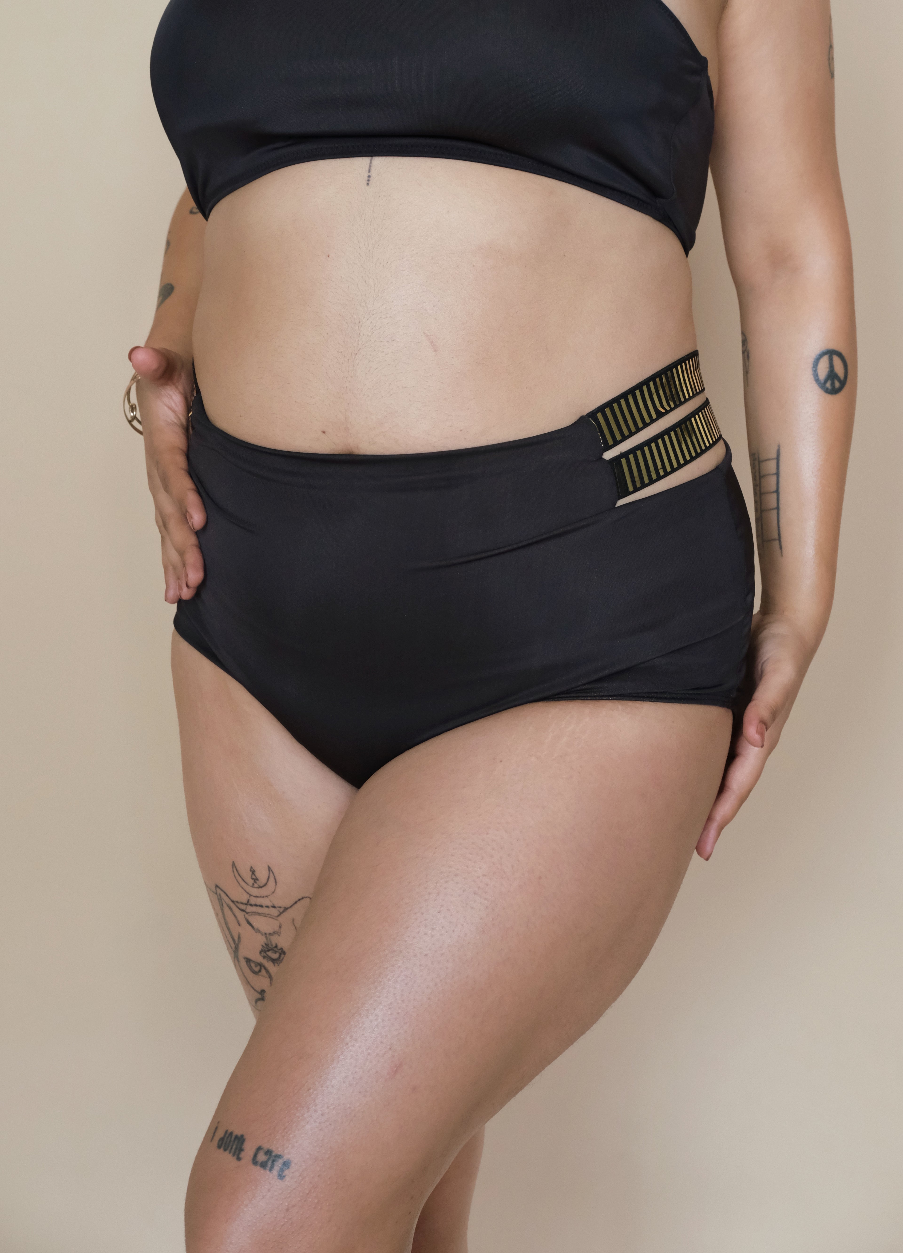 Woman wearing black high-waisted bikini bottoms with a beige background