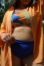 Woman wearing a colorful top and blue shorts with an orange shirt over it