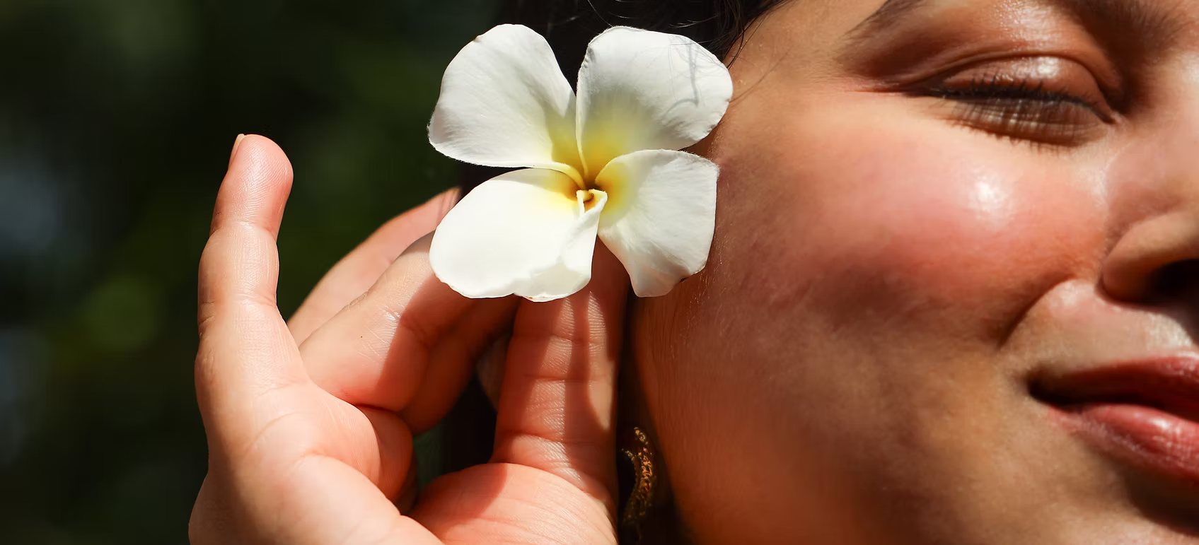Person holding a white flower close to their face with a blurred natural background